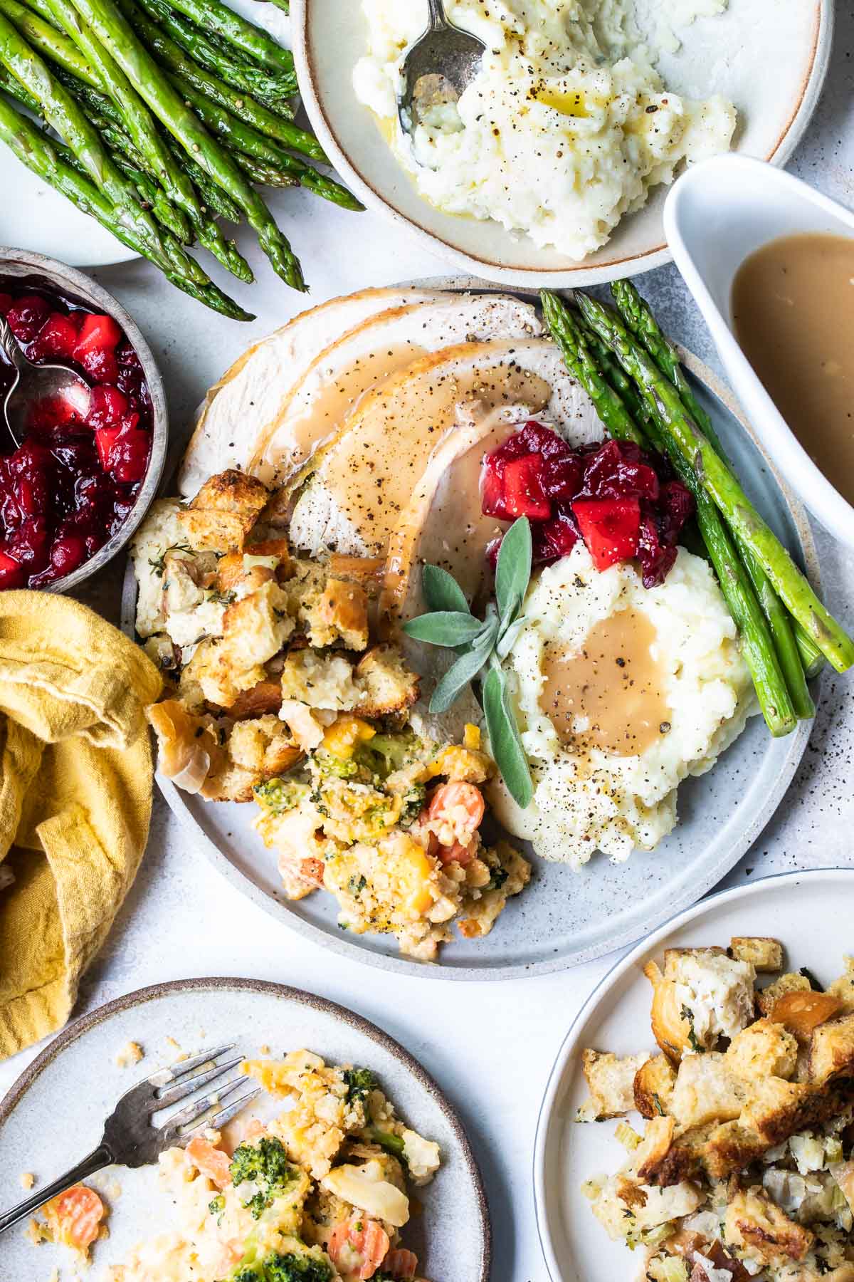 A plate of roasted trukey, stuffing, vegetables, mashed potatoes and gravy, and cranberries.