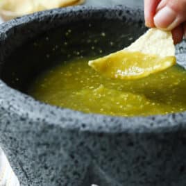 Someone dipping a chip into a molcajete with salsa verde inside.