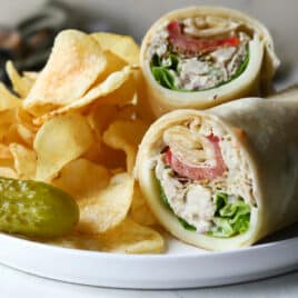 A tuna wrap on a plate with chips and a pickle.
