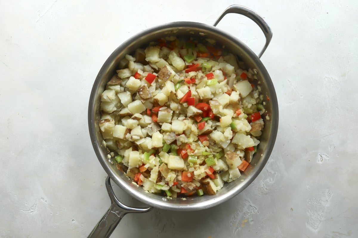 Potatoes, peppers, and onions cooking in a skillet (start of cooking).