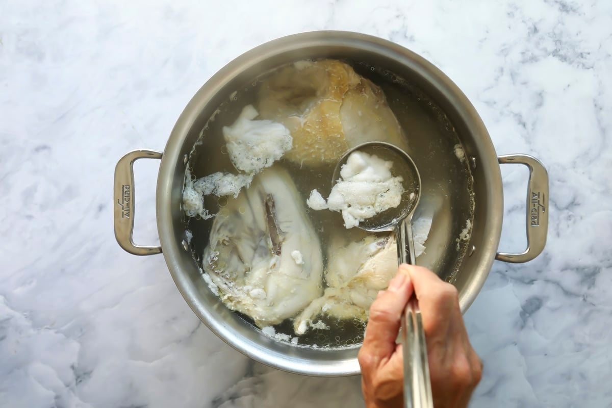 Someone skimming foam off a pot of chicken broth.