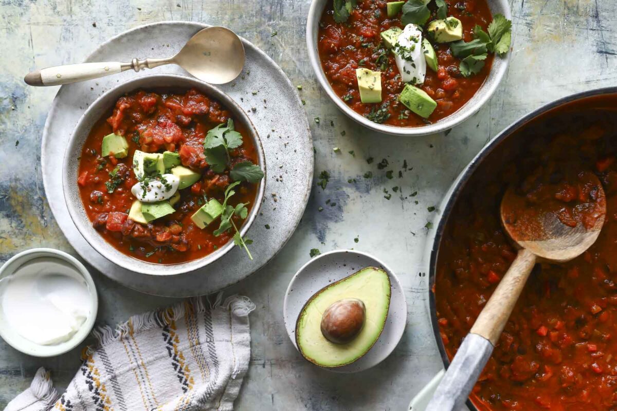 A bowl of pumpkin chili with sour cream, avocado, and cilantro on top.