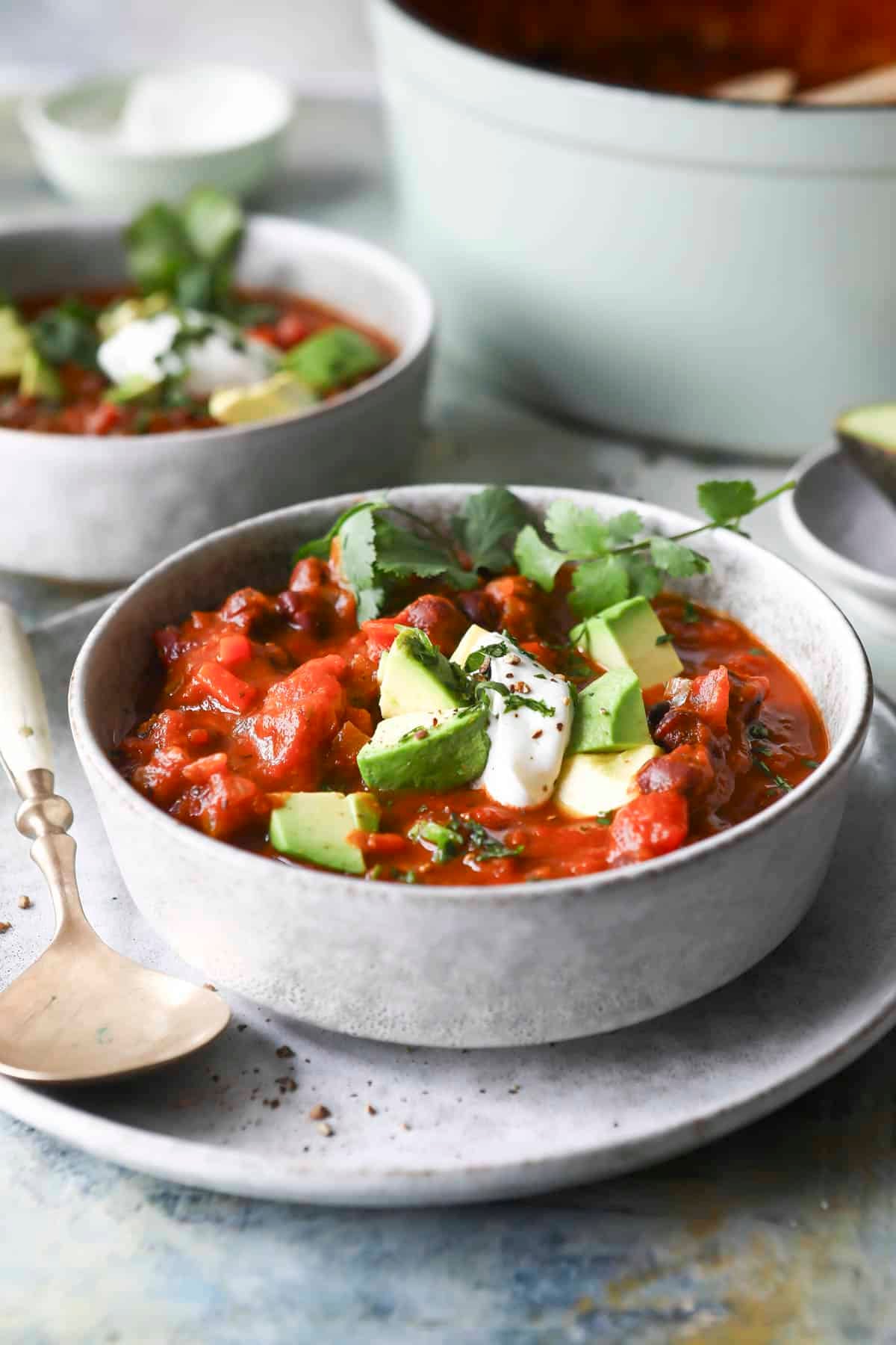 A bowl of pumpkin chili with sour cream, avocado, and cilantro on top.