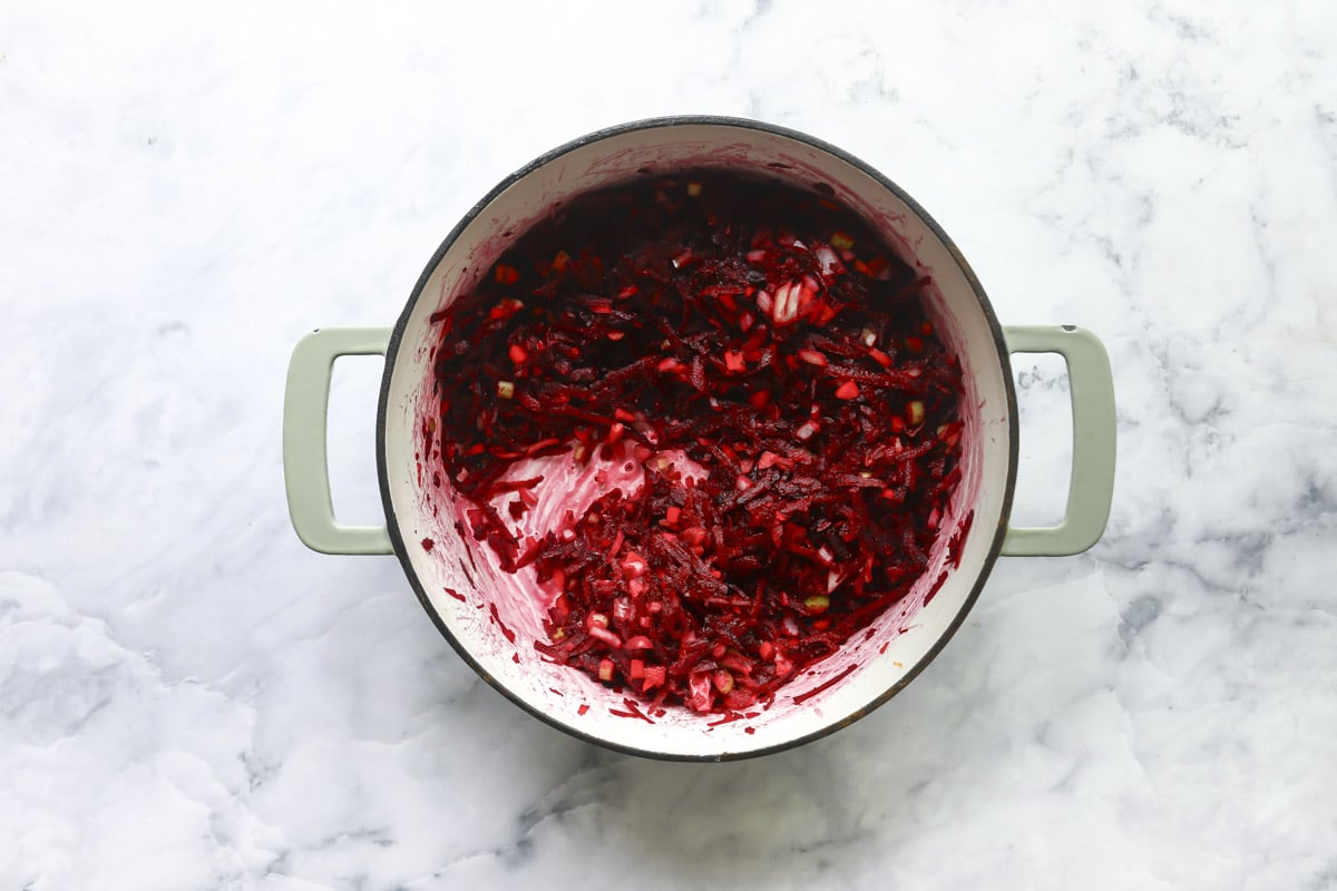 Grated beets and other vegetables cooking in a pot.