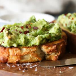A slice of toast slathered with mashed avocado and sprinkled with red chili flakes.
