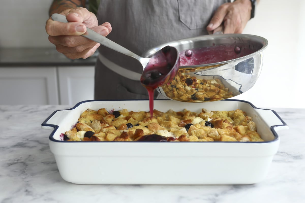 Pouring blueberry topping over a French toast casserole.