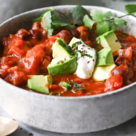 A bowl of pumpkin chili with sour cream, avocado, and cilantro on top.