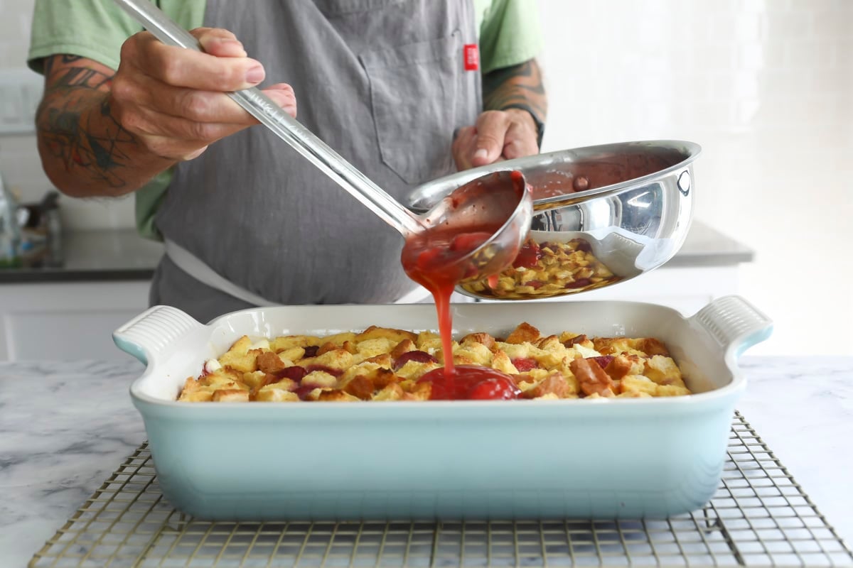 Pouring strawberry topping over a French toast casserole.