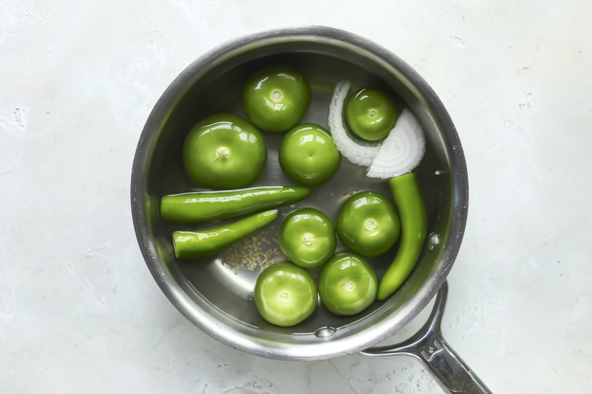 Tomatillos, serranos, onions, and garlic in a pot with water to boil for salsa verde.